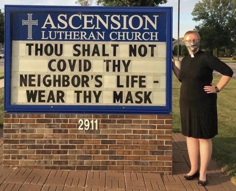Woman with a mask next to sign that reads do not covet thy neighbors life - wear thy mask