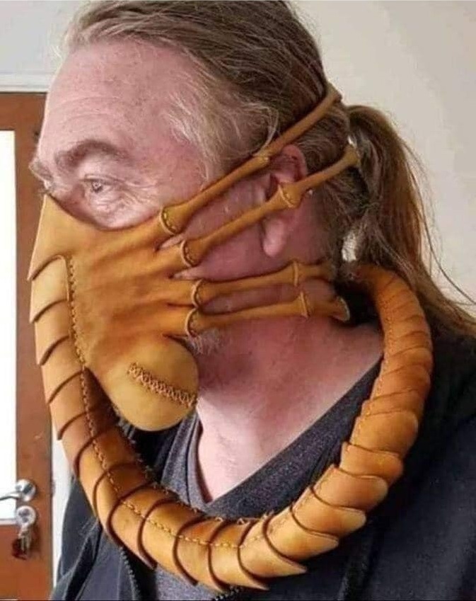 Middle-aged man with a pony tail wearing a mask that looks like an Alien-style facehugger